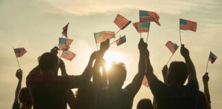 People holding and waving American flags at sunset sky