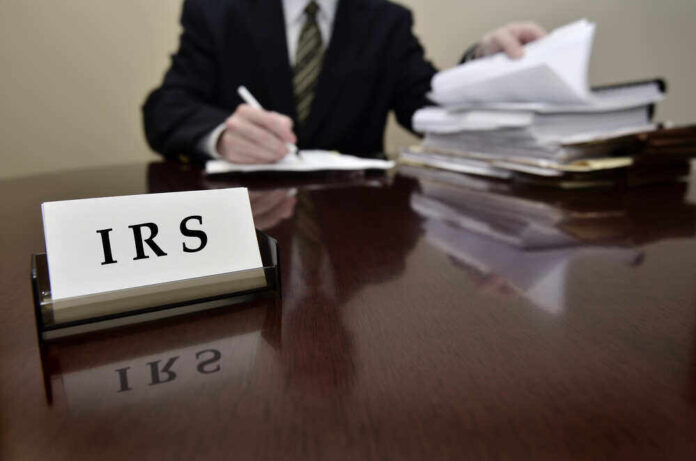 shutterstock_158874281.jpg featured image IRS sign on desk, person handling paperwork behind.