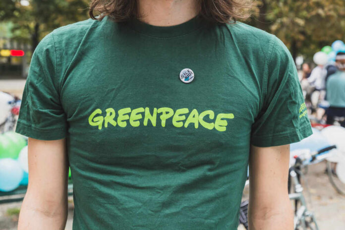 shutterstock_221491771.jpg featured image Person wearing green Greenpeace Tshirt with pin