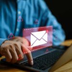 Person typing on laptop with mail warning icons.