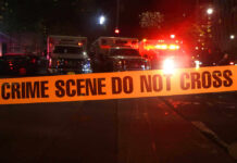 Crime scene tape with emergency vehicles in background.