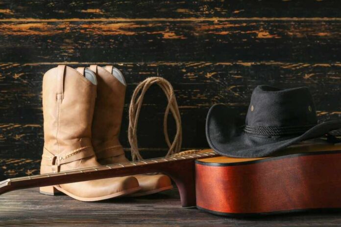shutterstock_2338150313.jpg featured image Cowboy boots, hat, and guitar on wooden surface.