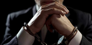Handcuffed person in suit, hands clasped together.