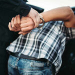 Crackdown STRIKES – Hundreds Arrested Nationwide! Person in handcuffs arrested by police officer.