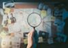 Magnifying glass over investigation board with photos and strings.