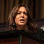 Sheriff Takes Kamala to the Woodshed! A woman speaking at a podium, looking serious.