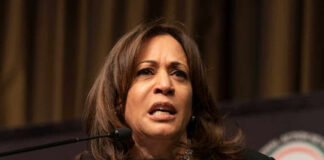 A woman speaking at a podium, looking serious.
