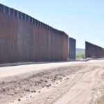 Dirt road beside tall metal border wall