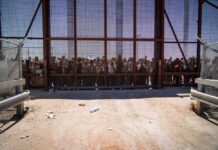 People standing behind a fence on a dusty path.