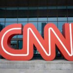 Red CNN logo in front of glass building.