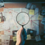 Magnifying glass over investigation board with photos and strings