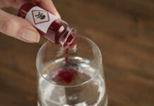 A close-up of a hand pouring poison into a glass of water