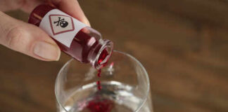 A close-up of a hand pouring poison into a glass of water