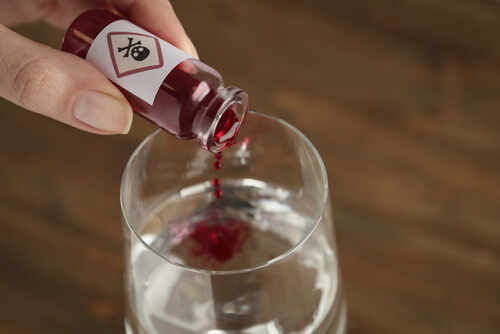 A close-up of a hand pouring poison into a glass of water