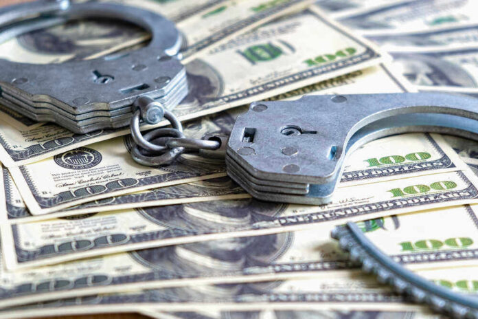 shutterstock_1934311637.jpg Handcuffs on a pile of one hundred dollar bills
