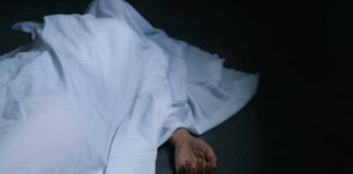 Hand emerging from under white sheet on dark surface.