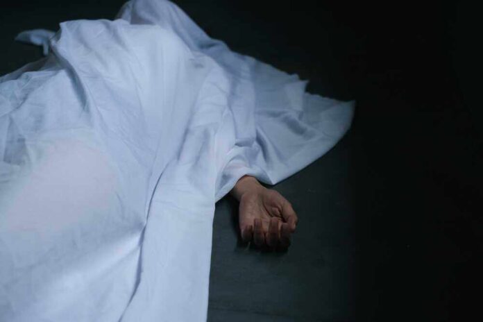 Hand emerging from under white sheet on dark surface.