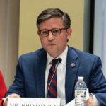 Mike Johnson in a suit speaks into a microphone.