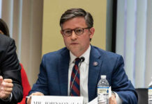 Mike Johnson in a suit speaks into a microphone.