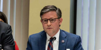 Mike Johnson in a suit speaks into a microphone.