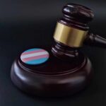 Gavel with transgender flag badge on black surface