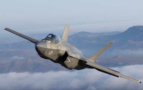 shutterstock_2595000113.jpg F-35 fighter jet flying above clouds with mountains in the background