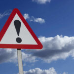 Warning sign with exclamation mark and blue sky background.