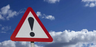 Warning sign with exclamation mark and blue sky background.