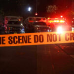 Crime scene tape with emergency vehicles in background.