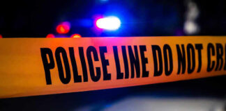 Police tape with flashing lights in the background