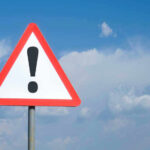 Triangle warning sign with exclamation mark against sky