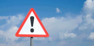 Triangle warning sign with exclamation mark against sky