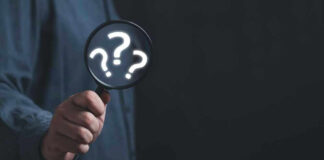 Hand holding magnifying glass with question marks