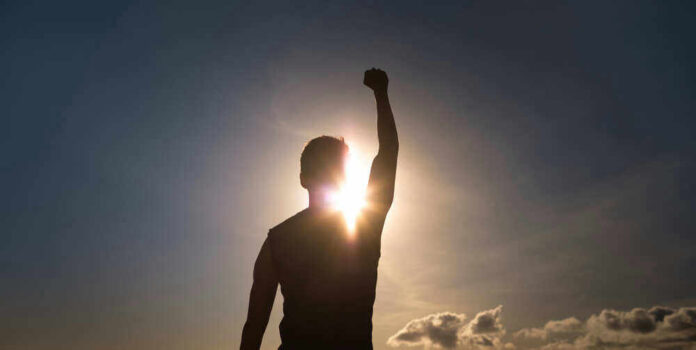 Silhouette of person with raised fist against sunset.