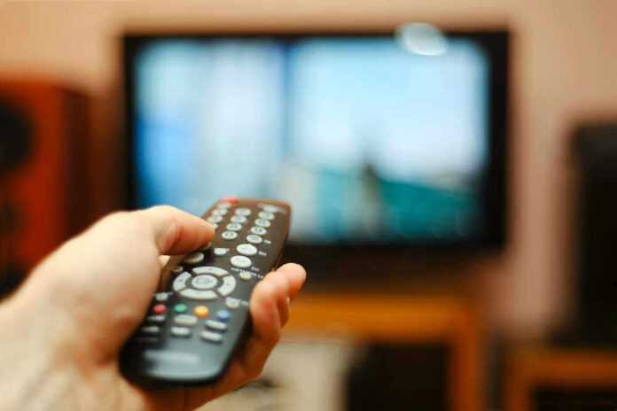 Hand holding a remote control towards a TV screen.