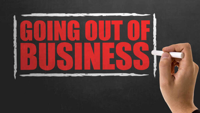 A hand writing 'GOING OUT OF BUSINESS' on a chalkboard