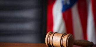 A wooden gavel resting on a sound block with an American flag in the background