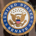 Famous Sports Reporter Announces Senate Run United States Senate seal with microphones in front.
