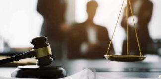 Gavel and scales in courtroom with blurred figures behind.