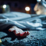 Crime scene with covered body and hand exposed.
