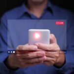 Streaming Giant’s GREED Targets Struggling Households Person holding a smartphone with a live streaming interface