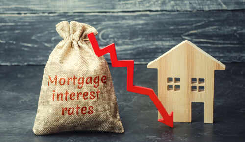 A burlap sack labeled Mortgage interest rates next to a wooden house and a downward red arrow