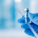 Vaccine Rulebook Shattered — States Revolt A gloved hand holding a syringe and a vial of liquid