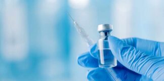 A gloved hand holding a syringe and a vial of liquid