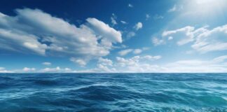 A vast ocean under a clear blue sky with scattered clouds