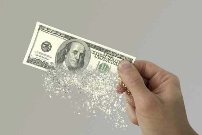 Hand holding a disintegrating hundred dollar bill.