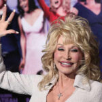 Person with blonde hair waves at an event.