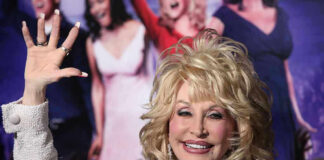 Person with blonde hair waves at an event.