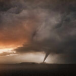 A tornado forming under dark storm clouds at sunset
