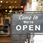 A black sign with white text that says 'Come In We're OPEN'